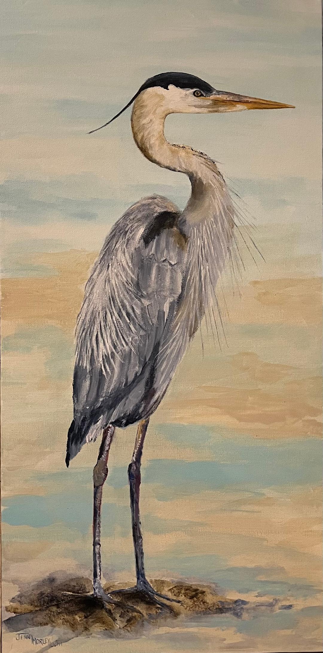 A great blue heron standing on a sandbar in profile, its plume feathers trailing, against a pale sky.