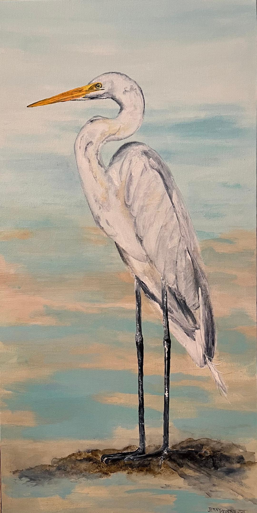 A white heron standing on a sandbar, neck curved and yellow bill raised, against a soft peach and blue sky.