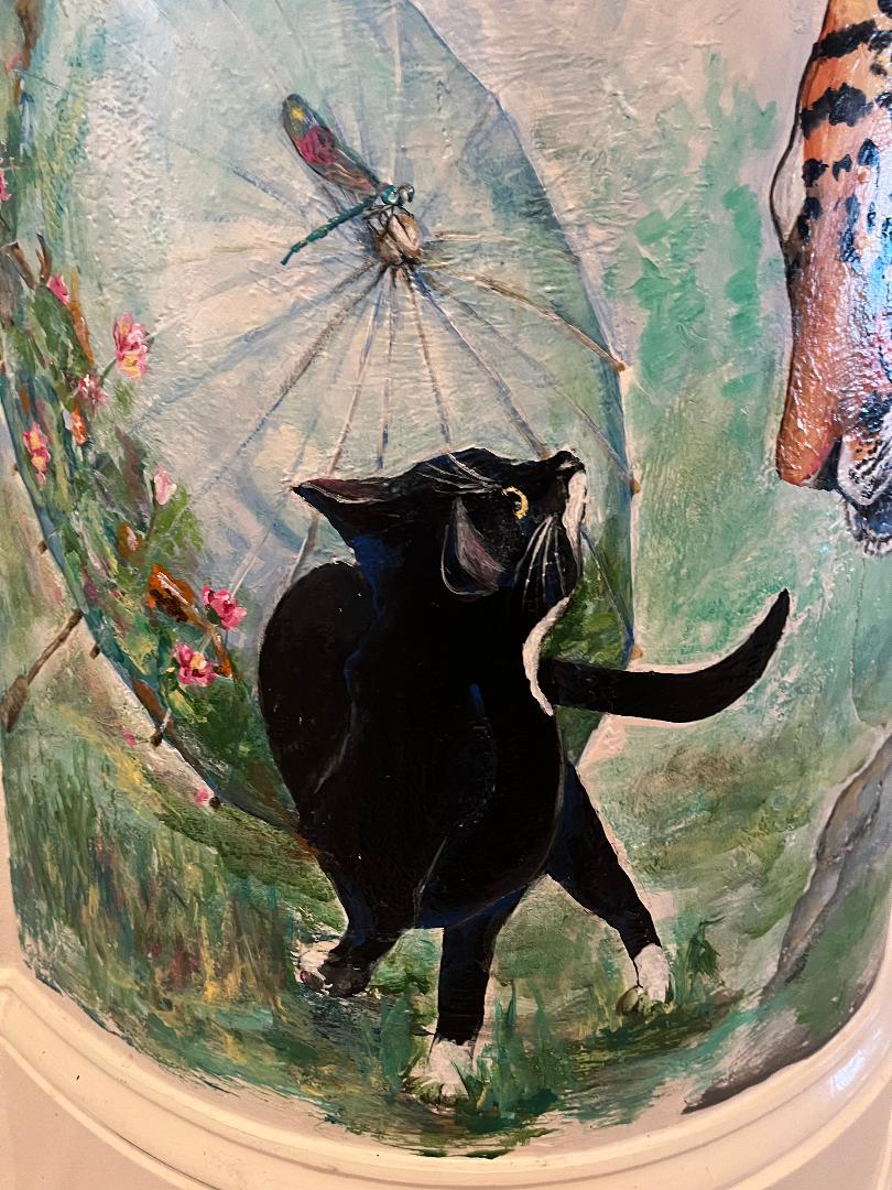 A black cat looking up at a dragonfly resting on an open parasol, painted on the curve of a column.