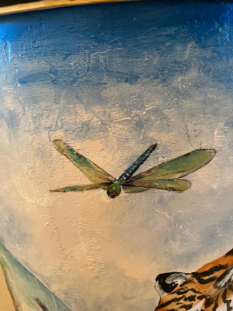 A translucent green dragonfly painted on a soft blue and white sky, with the back of a tiger just visible below.