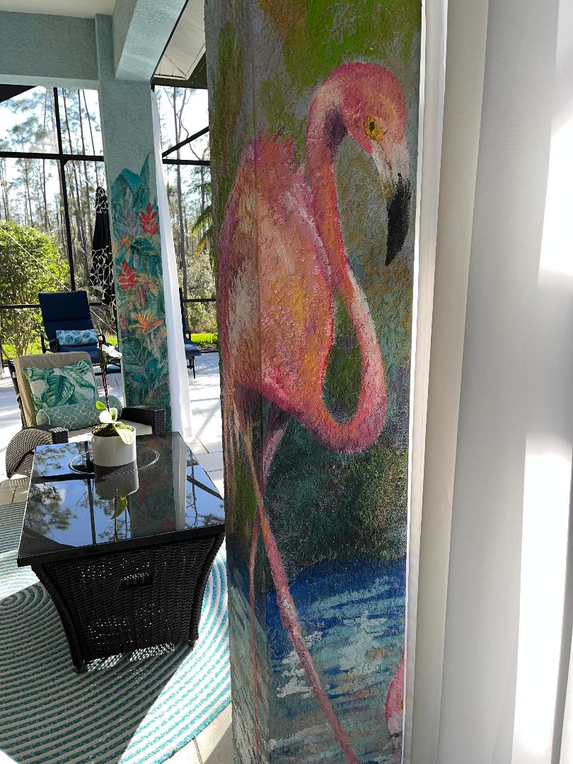 A pink flamingo painted the full height of a screened lanai column, with tropical foliage on the column beyond.