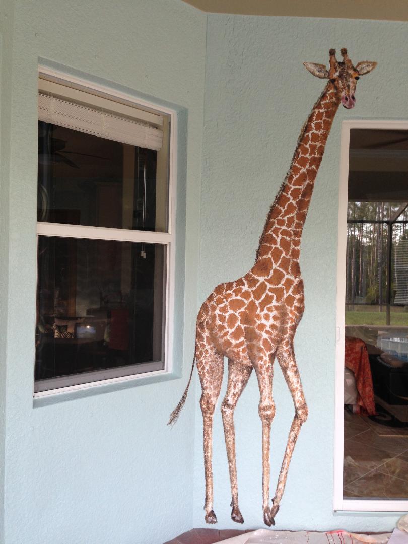 A giraffe painted floor to ceiling on a pale blue exterior lanai wall, between a window and a slider.
