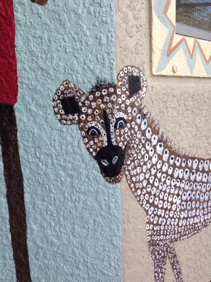 A spotted leopard painted around an exterior wall corner, head turned toward the viewer.