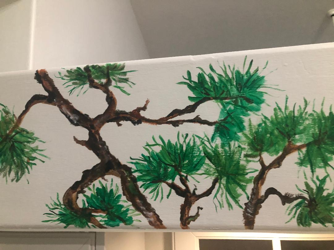 Twisting pine branches and needle clusters painted along a white interior ceiling beam.