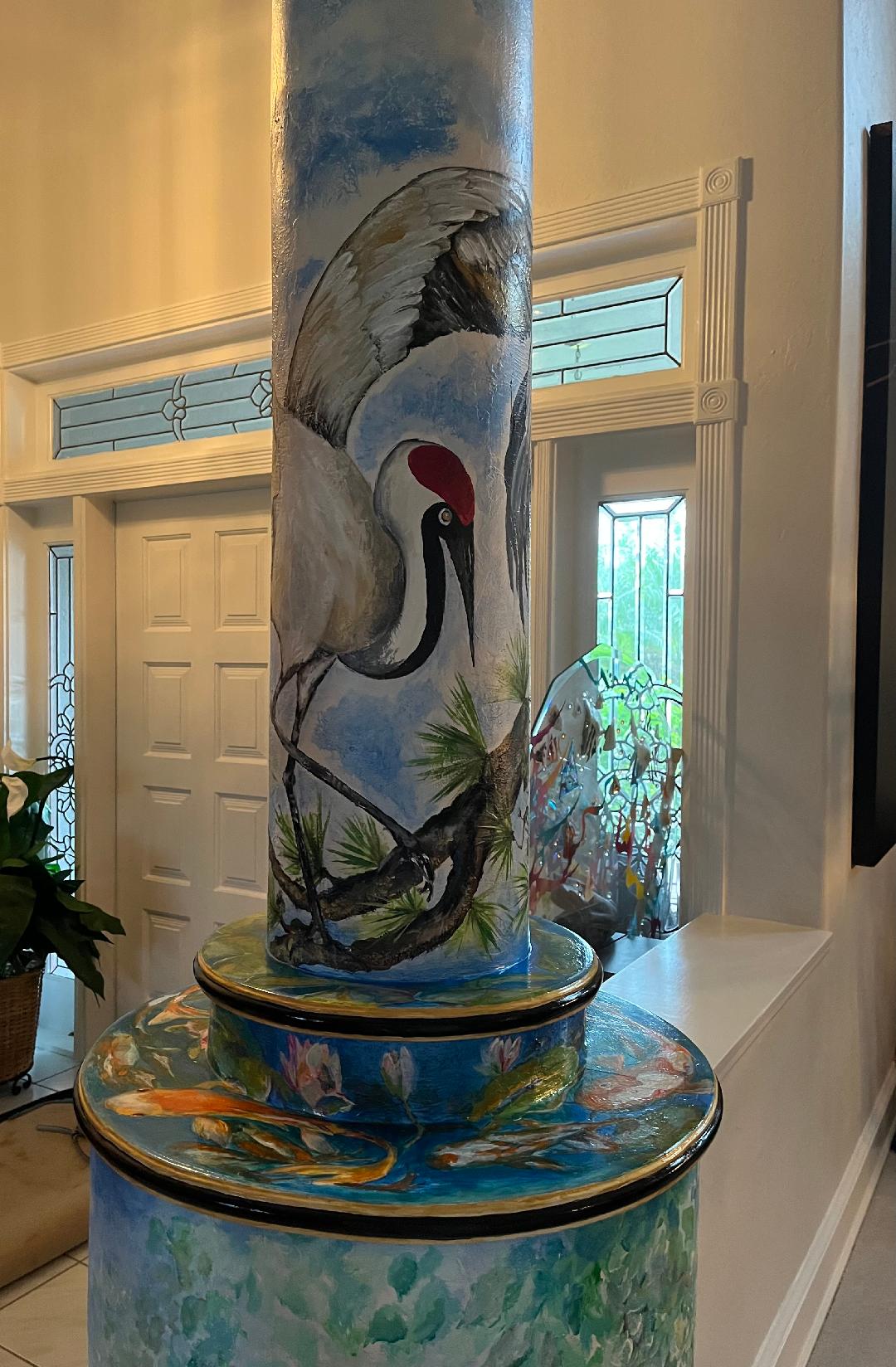 An entryway column painted with a life-size sandhill crane wading among pine branches, its stepped base painted as a koi pond.