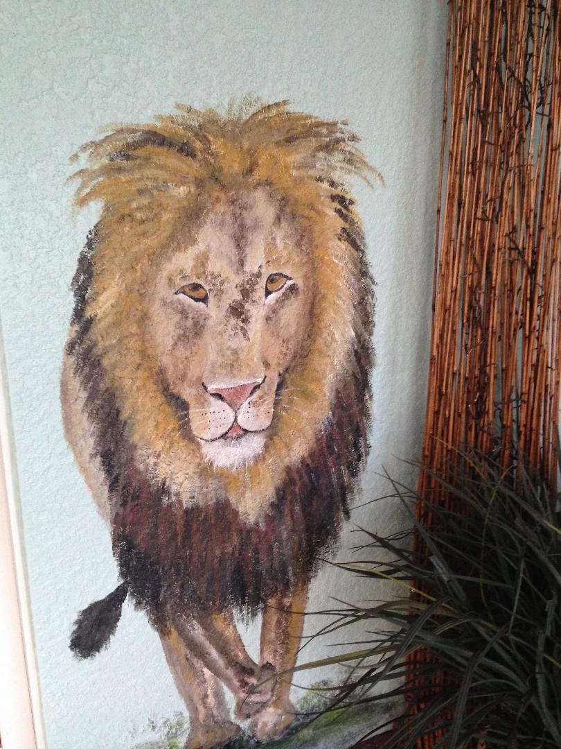 A lion walking out of a pale interior wall at close to life size, its mane worked in dry-brushed golds and browns.