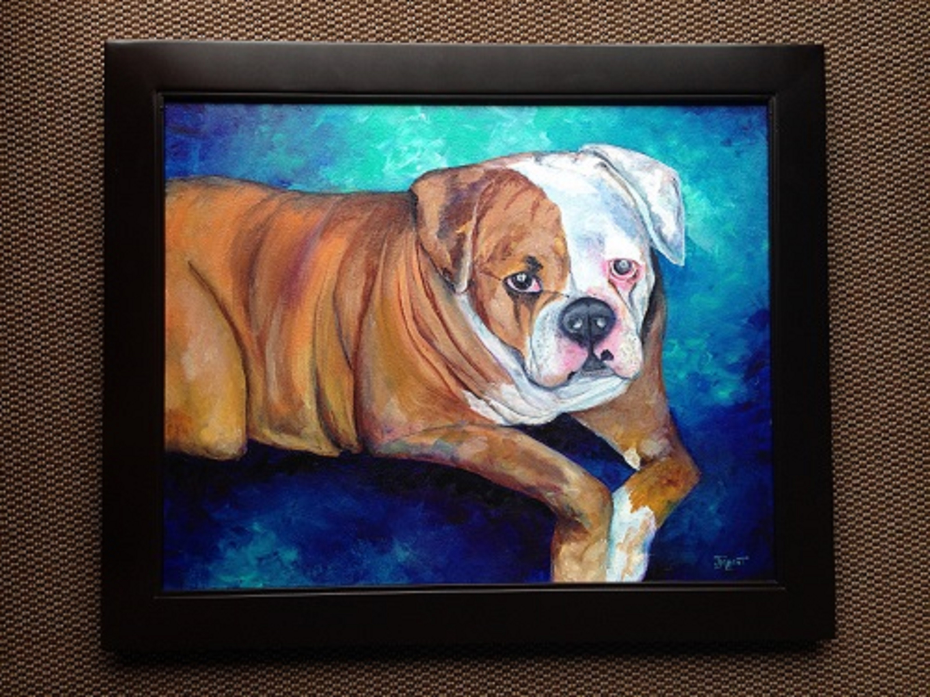 A tan and white bulldog lying down and looking straight at the viewer, painted against turquoise and deep blue, in a black frame.