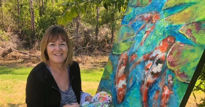 Jenny Morley Licht standing outdoors beside an easel holding a large koi painting, palette in hand.