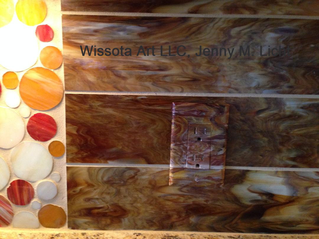 An electrical outlet cover hand-painted to disappear into the swirled amber and rust glass tile around it.