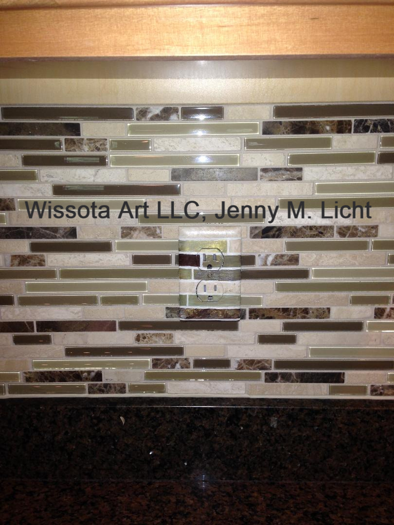 An outlet cover painted to match a linear mosaic backsplash of cream, bronze and stone.