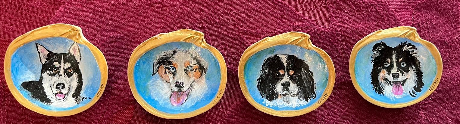 Four shell ornaments in a row, each painted with a different dog's head on a pale blue ground and edged in gold.